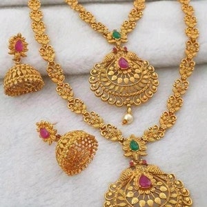 May include: A gold necklace set with two pendants, each featuring intricate floral designs and pink and green gemstones. The set also includes matching earrings with a similar design.