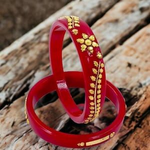 May include: Two red bangles with gold leaf designs. The bangles are stacked on top of each other.