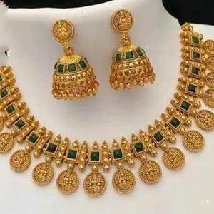 May include: A gold necklace with green stones and a matching pair of earrings. The necklace features a design of small round coins with a deity figure on each coin.