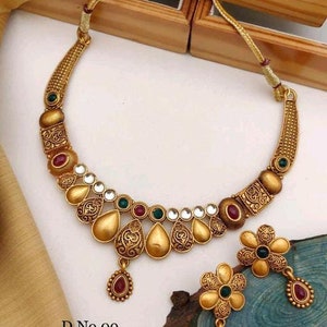 May include: A gold necklace and earrings set with a floral design and red and green stones. The necklace has a pendant with a teardrop shape. The earrings are small and have a flower shape. The text on the image reads "D.No.09 Met Gold Fancy Designer Necklace".