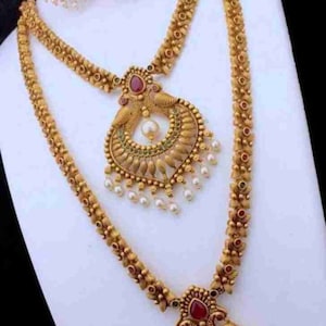 May include: A gold-tone necklace set with a peacock design. The necklace has two strands, one shorter than the other. The pendant features a red stone and pearl accents. The earrings are also gold-tone and feature a peacock design with red stones.