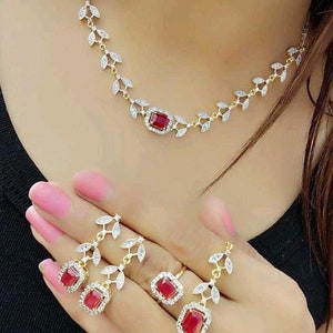 May include: A gold-toned jewelry set featuring a necklace, earrings, ring, and bracelet. Each piece has a leaf-like design with clear crystals and a central, rectangular, red gemstone. The bracelet is adjustable.