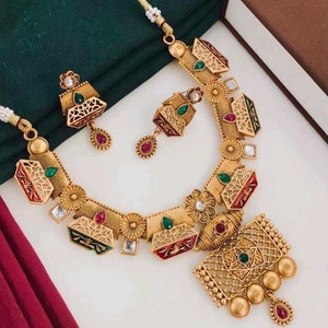 Könnte beinhalten: Ein goldfarbenes Halsketten- und Ohrring-Set mit filigranen Designs und bunten Emaille-Akzenten. Die Halskette hat einen Anhänger mit einem geometrischen Muster und die Ohrringe sind in Form von kleinen Kästchen mit floralen Details gestaltet.