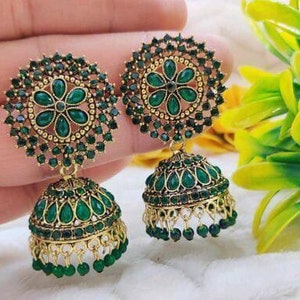 May include: A pair of gold-tone earrings with green gemstone accents. The earrings feature a round, floral design with a dangling bell-shaped charm.