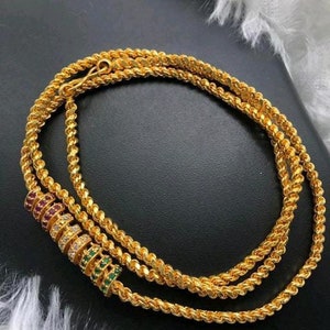 May include: A gold chain necklace with a decorative charm featuring green, red and white stones.