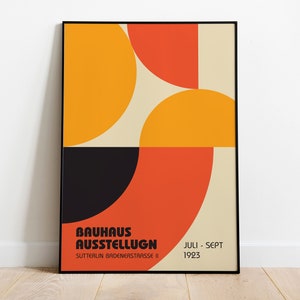 Puede incluir: Un póster enmarcado en negro con un diseño geométrico en naranja, amarillo y negro. El texto del póster dice "Bauhaus Austellung" y "Sutterlin Brudernerstrasse II" y "Juli - Sept 1923".