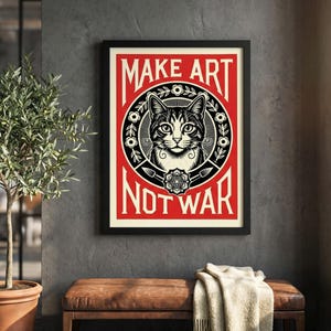 以下が含まれることがあります： 赤い背景に「MAKE ART NOT WAR」の白い文字が入った額入りのアートプリント。このアートワークは、猫の顔の精巧な白黒イラストを特徴としています。このプリントは灰色の壁に飾られています。