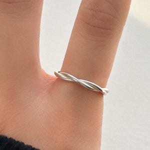 Puede incluir: Un anillo plateado con un diseño de cuerda trenzada. El anillo se lleva en un dedo, mostrando su patrón delicado e intrincado. El diseño del anillo es simple pero elegante, adecuado para el uso diario.