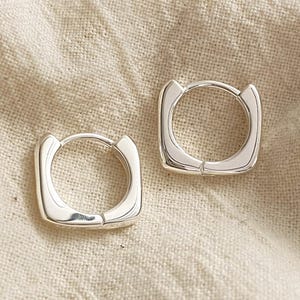 May include: A pair of silver square hoop earrings. The earrings are simple and modern in design.
