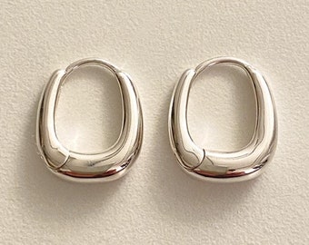 May include: A pair of silver hoop earrings with a rounded, oval shape.
