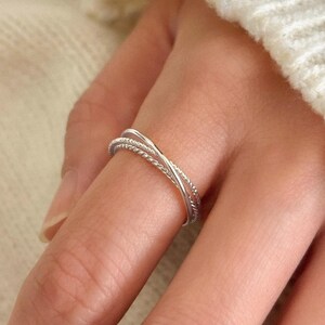 Sterling silver stacking ring made of three interlocking bands, each with a unique texture, forming a delicate trinity-style design.