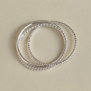 Thin 1mm silver rings linked together in a fluid, sculptural form with mixed textures including smooth, twisted, and rope styles.
