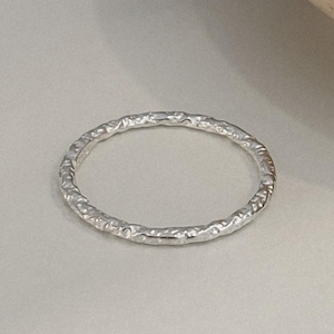 May include: A silver ring with a textured surface. The ring is circular and appears to be made of metal. The ring is a simple band design, suitable for everyday wear.