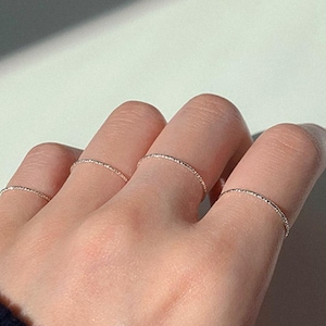 Może przedstawiać: Ręka z kilkoma cienkimi srebrnymi pierścionkami. Pierścionki są ułożone na palcach i są bardzo delikatne.