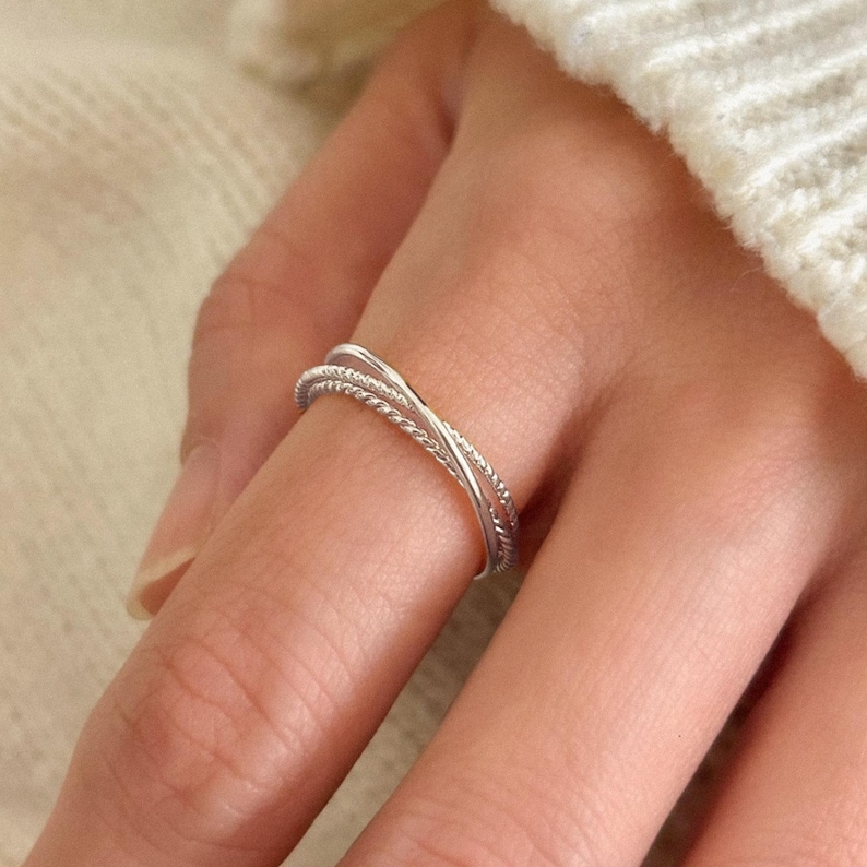 Sterling silver stacking ring made of three interlocking bands, each with a unique texture, forming a delicate trinity-style design.