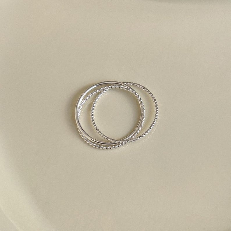 Thin 1mm silver rings linked together in a fluid, sculptural form with mixed textures including smooth, twisted, and rope styles.