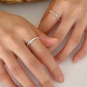 Three slim sterling silver bands with mixed textures—smooth, twisted, and rope—interlocked into one fluid stacking ring for everyday elegance.