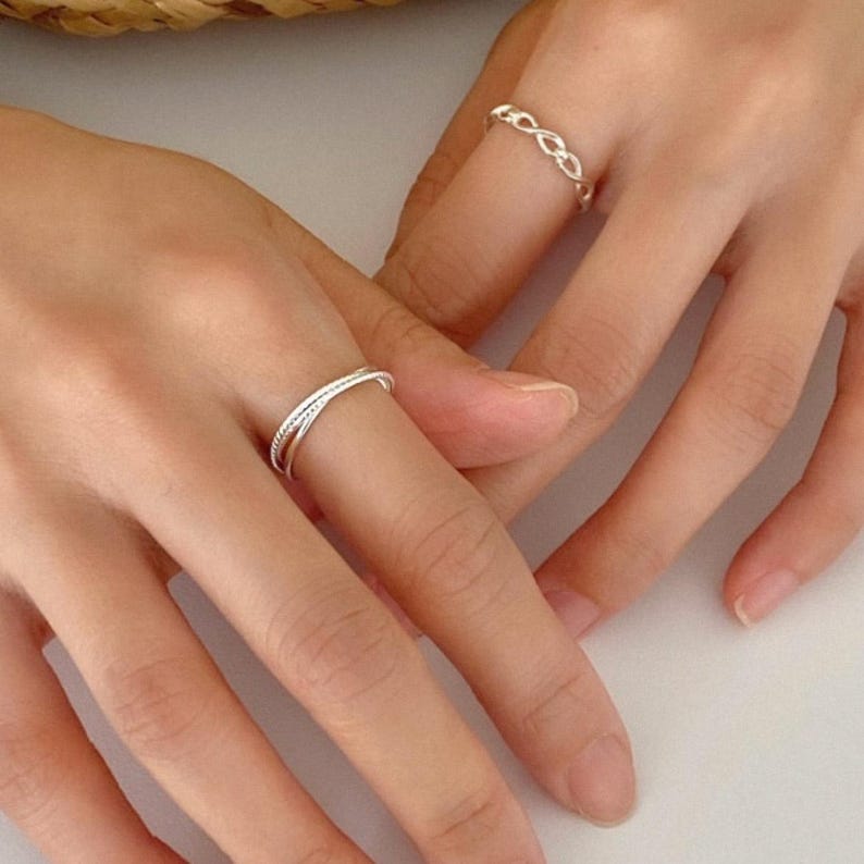 Three slim sterling silver bands with mixed textures—smooth, twisted, and rope—interlocked into one fluid stacking ring for everyday elegance.