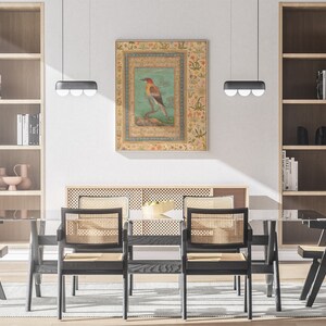 May include: A dining room with a black wooden table and chairs. The chairs have woven cane seats and backs. A framed artwork of a colorful bird on a branch hangs on the wall above the table. The artwork has a gold frame and a floral border.
