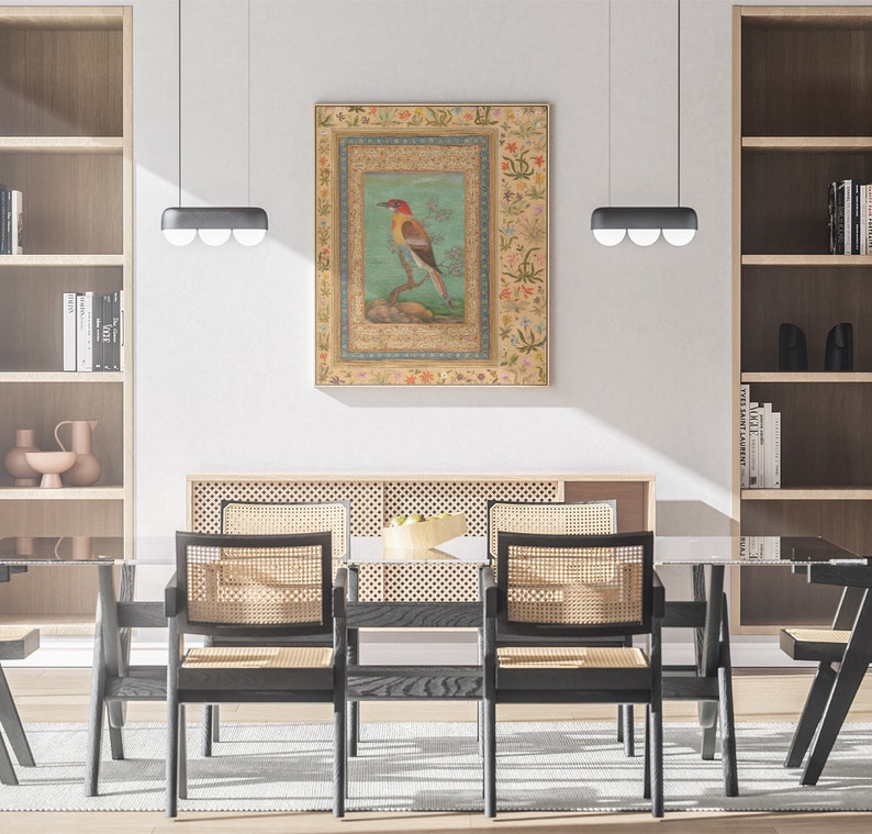 May include: A dining room with a black wooden table and chairs. The chairs have woven cane seats and backs. A framed artwork of a colorful bird on a branch hangs on the wall above the table. The artwork has a gold frame and a floral border.