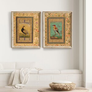 May include: Two framed prints with ornate gold frames and intricate floral borders. The prints feature detailed illustrations of birds, one a pheasant and the other a colorful bird with a long beak, on a light blue background.