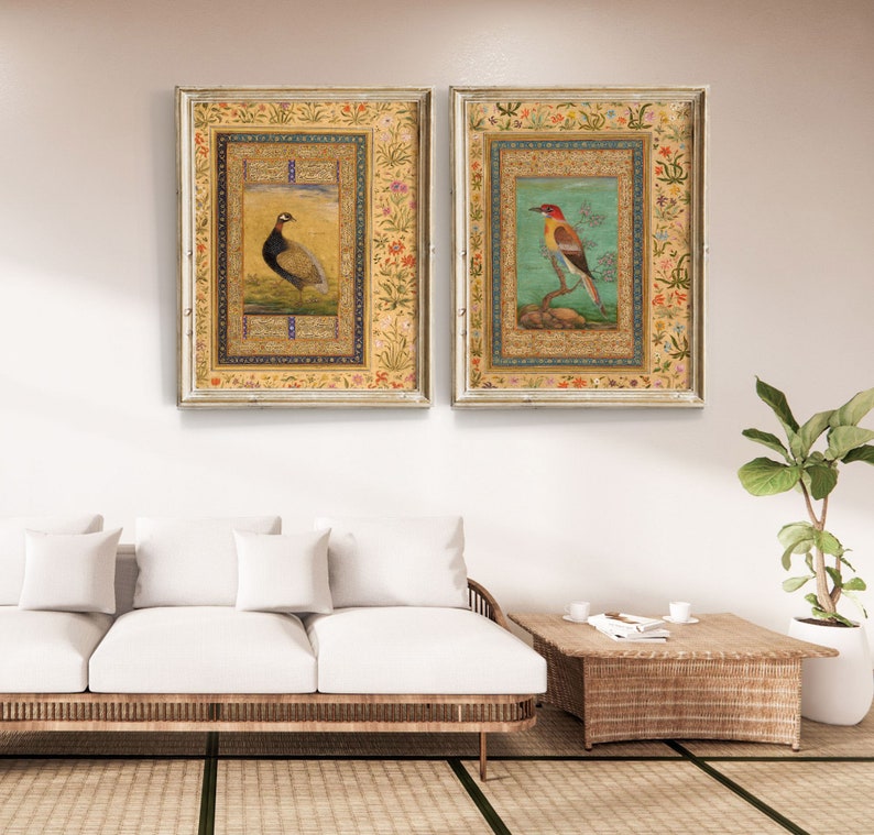 May include: Two framed paintings with ornate gold frames. The paintings feature detailed illustrations of birds on a light blue background with intricate floral borders.