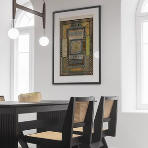 Puede incluir: Una impresi&oacute;n enmarcada en negro de una ilustraci&oacute;n vintage de un patr&oacute;n geom&eacute;trico. La impresi&oacute;n est&aacute; colgada en una pared blanca sobre una mesa de comedor negra con dos sillas negras con asientos de ca&ntilde;a tejidos.