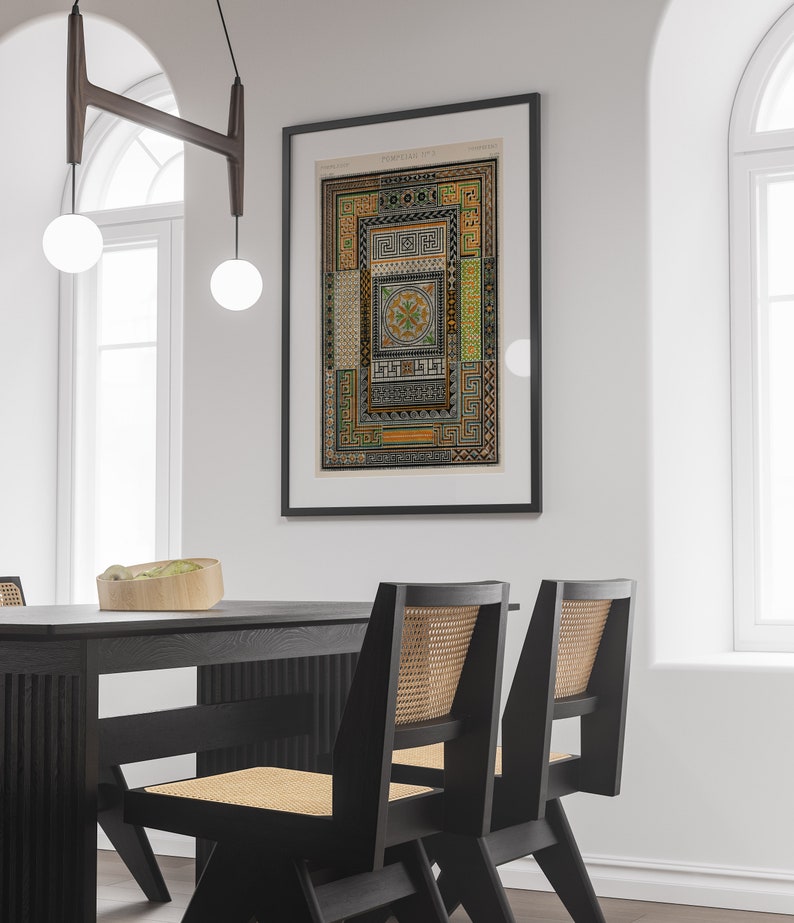 Puede incluir: Una impresi&oacute;n enmarcada en negro de una ilustraci&oacute;n vintage de un patr&oacute;n geom&eacute;trico. La impresi&oacute;n est&aacute; colgada en una pared blanca sobre una mesa de comedor negra con dos sillas negras con asientos de ca&ntilde;a tejidos.