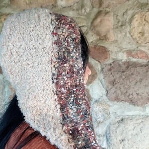 Può includere: Una sciarpa con cappuccio realizzata con due tipi diversi di filato. Un lato è in filato soffice color crema, l'altro lato è in filato maculato marrone, rosso e bianco.