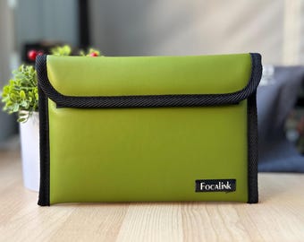 May include: A rectangular olive green pouch with a fold-over flap and black fabric trim along the edges. The pouch features a black rectangular label in the bottom right corner with the white text Focalink printed on it in a serif font.