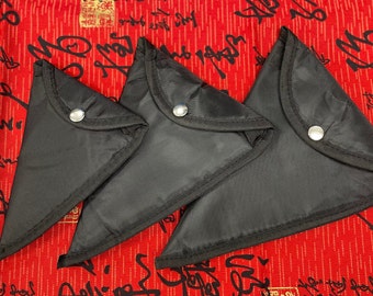 May include: Three black triangular pouches with silver snap closures are arranged on a red background with black calligraphy. The pouches are made of a smooth, matte material and have a simple, minimalist design.