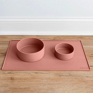 Pu&ograve; includere: Un set di due ciotole per cani in silicone rosa con un tappetino in silicone rosa abbinato. Le ciotole sono etichettate "Trough" e il tappetino &egrave; etichettato "Trough".