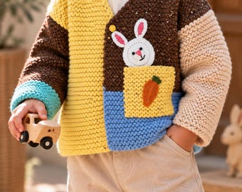 May include: A colour-blocked knit cardigan featuring a yellow right side, a brown left side with a white rabbit appliqué, and a yellow pocket with an orange carrot appliqué. The sleeves are brown, beige, and turquoise, with a V-neckline.