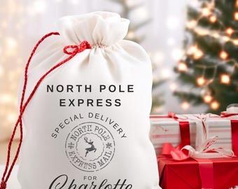 May include: White fabric gift bag with red drawstring, featuring the text "North Pole Express" and a black and white stamp with a reindeer and the text "Special Delivery North Pole Express Mail". The bag is personalized with the name "Charlotte".