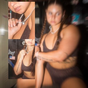 May include: A black sports bra and shorts set. The model is wearing a pearl necklace with a silver pendant. The image has a blurred effect. The model has long braids and tattoos on their arms.
