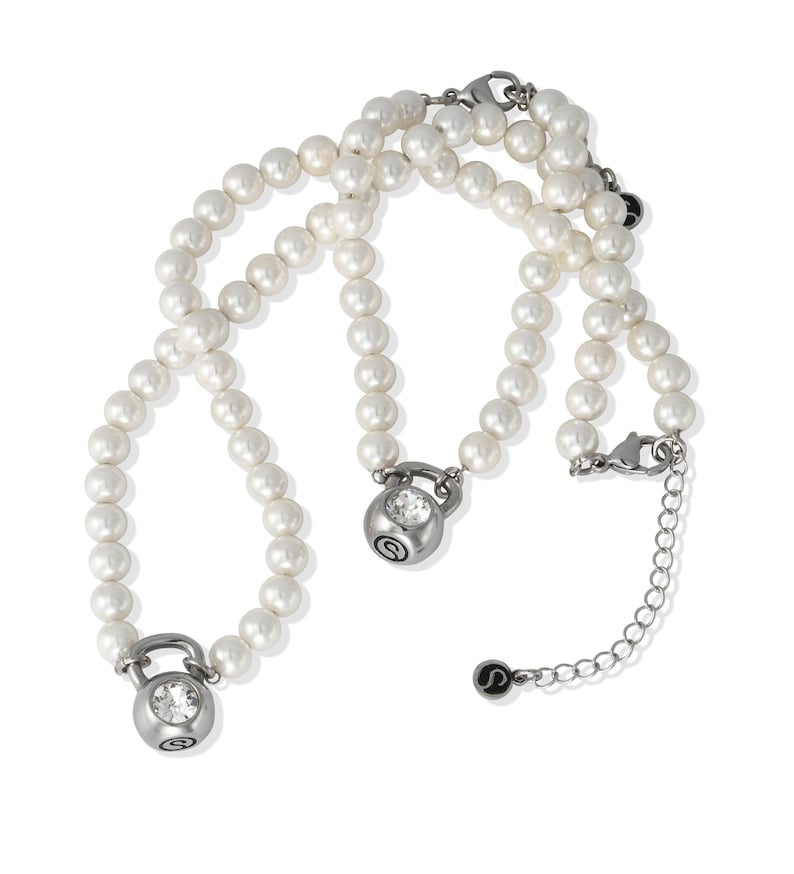 May include: A white pearl necklace with two silver-toned kettlebell pendants, each featuring a clear crystal. The necklace has a silver clasp and an extender chain. The pendants have a small, stylized "S" logo.