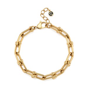 May include: A gold-colored chain bracelet with a lobster clasp closure. The bracelet features a series of rectangular links connected by smaller, rounded links. The bracelet has a small, circular charm with a black center and a gold-colored letter "S".