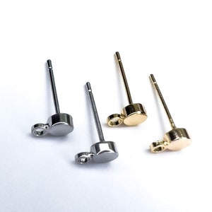 May include: Three earring posts with a small round charm attached to the end. The posts are silver, gold, and rose gold.