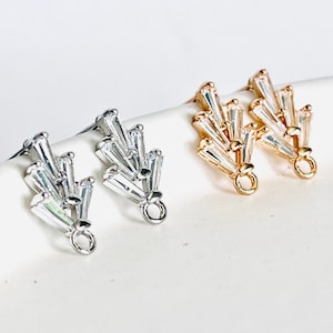 Peut inclure: Une paire de fermoirs de boucles d'oreilles avec une finition dorée et argentée. Chaque fermoir présente un groupe de cristaux clairs en forme de baguette.
