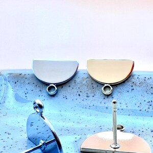 May include: Two silver half-circle earring blanks with a jump ring on the top and a post on the bottom.