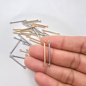 May include: Two jump rings, one gold and one silver, with a straight bar connecting the rings. The jump rings are held in a hand.