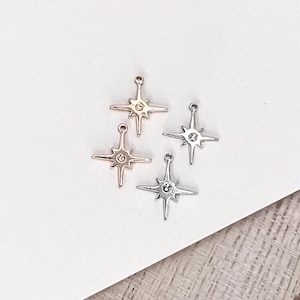 Pode incluir: Quatro pingentes em forma de estrela com um pequeno cristal transparente no centro. Dois pingentes são prateados, um é dourado e um é dourado rosa.