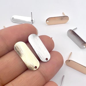 May include: Six oval-shaped earring blanks with a post and a hole at the top. The blanks are in silver, gold, and rose gold.