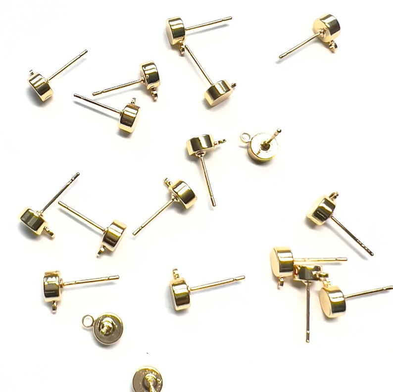 K&ouml;nnte beinhalten: Eine Gruppe von 14 goldfarbenen Ohrring-Findings mit rundem Kopf und gerader Stift. Die Findings haben eine &Ouml;se oben zum Anbringen eines Charms oder einer Perle.