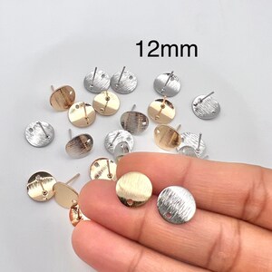 May include: A collection of 12mm round earring blanks in gold and silver tones. The blanks have a hole in the center for attaching earring posts.
