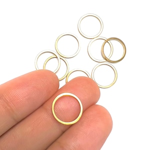 May include: A group of ten gold-coloured metal jump rings. The rings are all the same size and are arranged in a loose pile. One ring is being held by a finger.