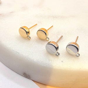 May include: Four stud earrings with a post and loop design. Two are gold-toned, and two are silver-toned. The earrings have a flat, circular face and are displayed on a white surface.