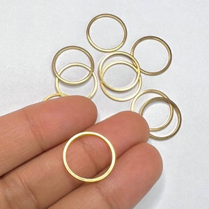May include: A group of gold-coloured metal jump rings, some are stacked on top of each other. The jump rings are approximately 2.5 cm in diameter.