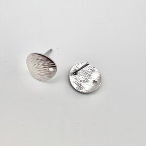 May include: Two silver-toned earring posts with a textured round disc. The discs have a small hole in the center.