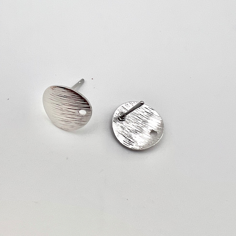 May include: Two silver-toned earring posts with a textured round disc. The discs have a small hole in the center.